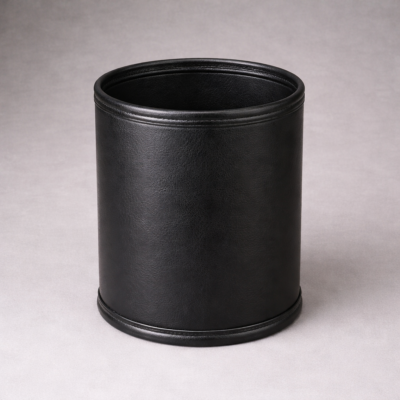 Round black leatherette wastebasket with smooth textured finish on a neutral background, suitable for hotel guest rooms and bathrooms.